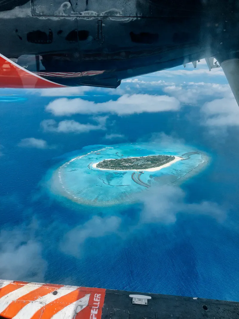 Small tropical island ringed by a turquoise reef seen from an aircraft window