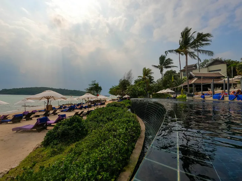 Infinity pool edge curving above the sand with beach loungers and umbrellas at Anantara Lawana