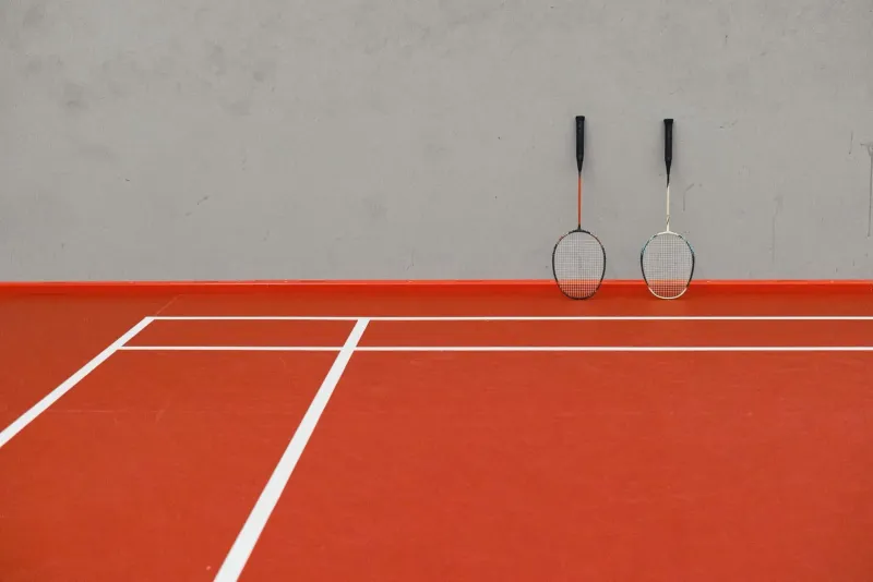 Two badminton rackets leaning against the wall of an empty red-floored indoor court