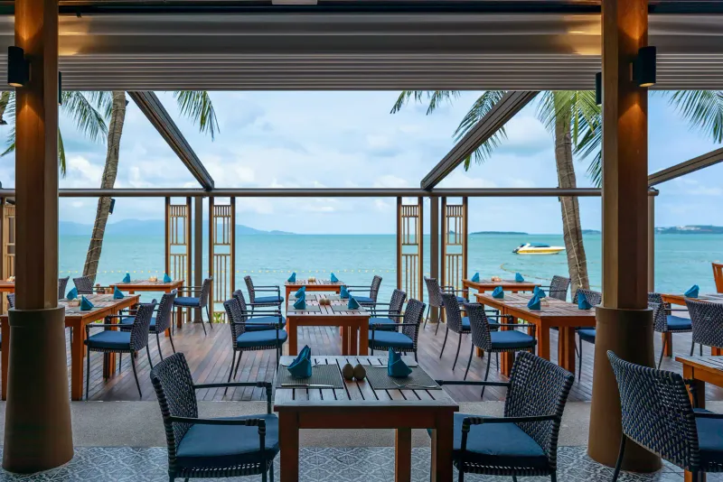 Chom Dao beach restaurant terrace at Bandara Resort Samui with rattan chairs and blue napkins facing the bay