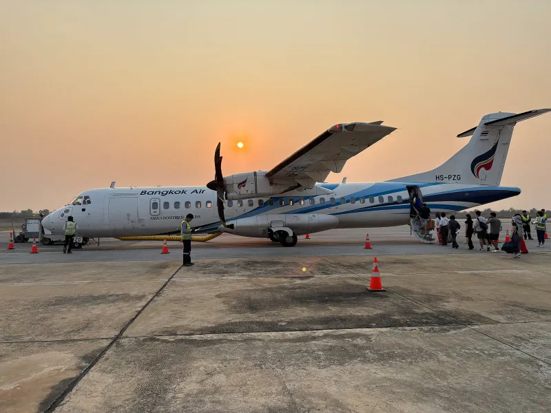 Passengers boarding a Bangkok Airways ATR 72-600 on an airport apron at sunset