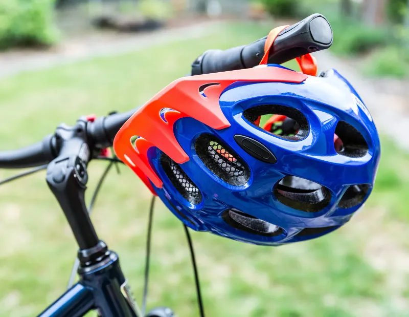 Blue and orange bicycle helmet hanging from the handlebars of a parked bike