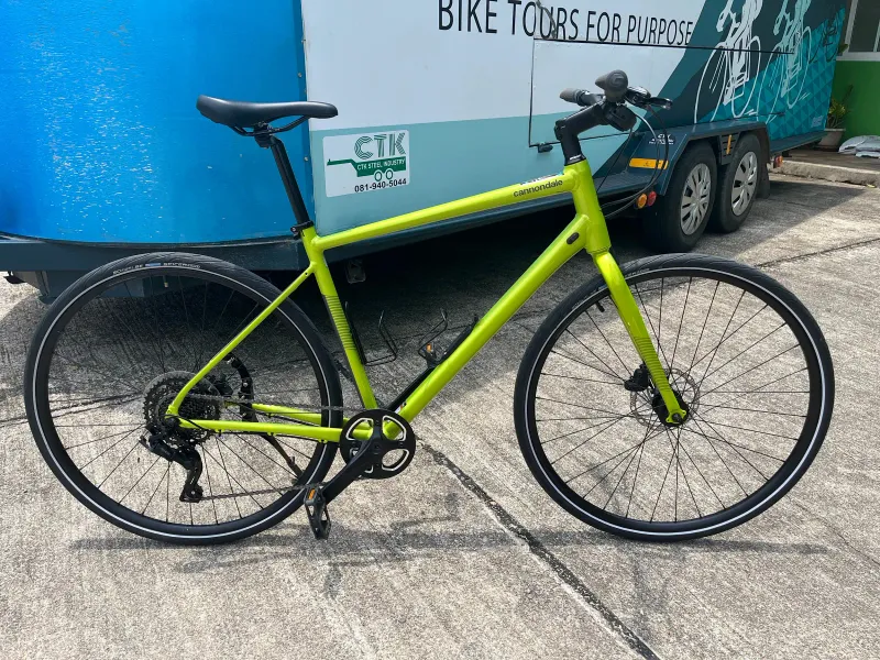 Lime green hybrid city bicycle with disc brakes parked on concrete beside a bike tour trailer