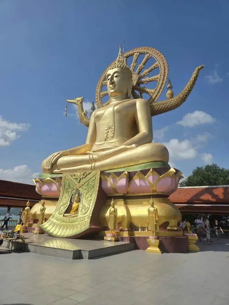 Low-angle view of the golden Big Buddha statue against a blue sky at Wat Phra Yai