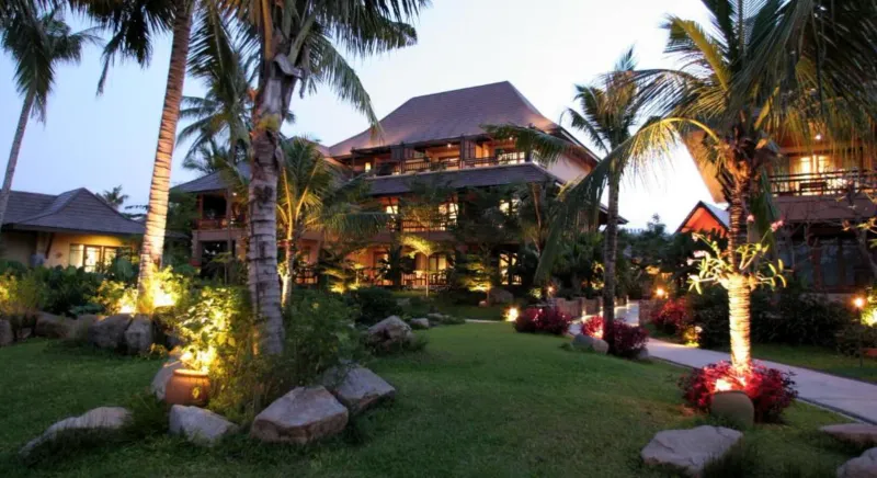 Evening lights on the lawn and palm garden of Bo Phut Resort and Spa with villa roofs behind