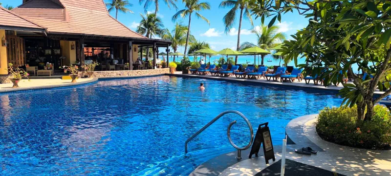 Large swimming pool at Bo Phut Resort and Spa with a Thai-roofed restaurant pavilion and palms by the bay