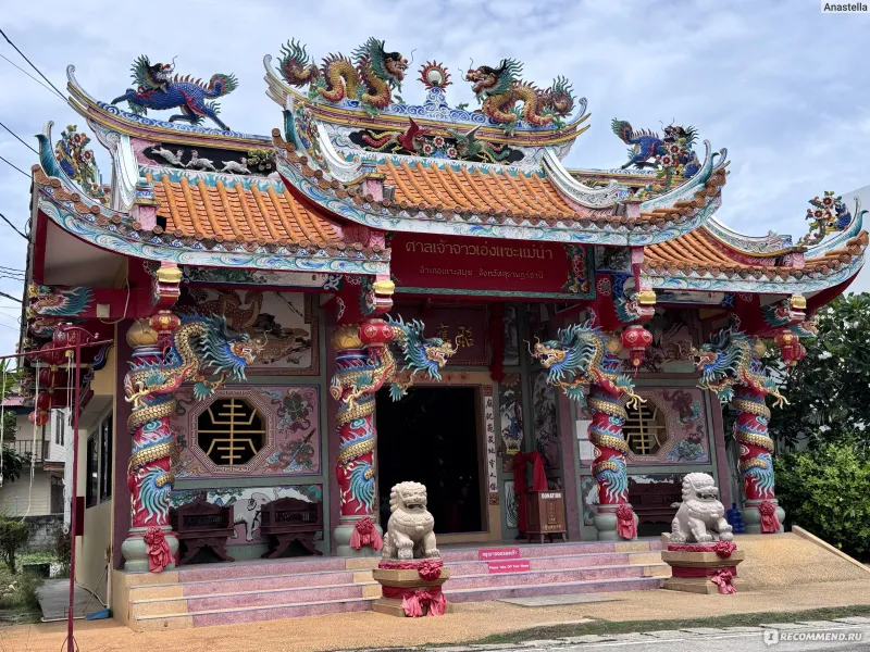 The shrine's dragon-topped roofline and stone lion guardians, with its Thai name painted above the entrance