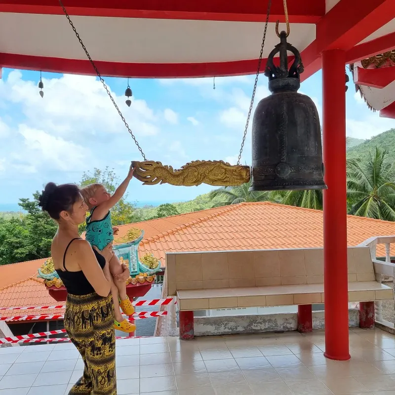 A large bronze bell hanging beneath a red pavilion roof at the shrine