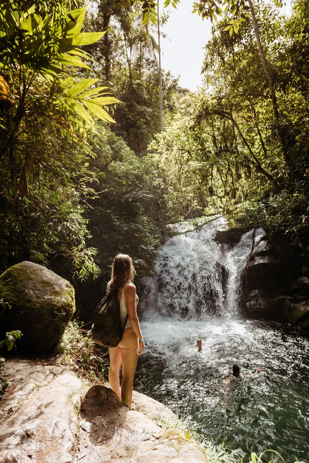 A hiker cools off in a shaded jungle waterfall pool, the kind of natural swimming spot found at the base of Tan Rua's falls