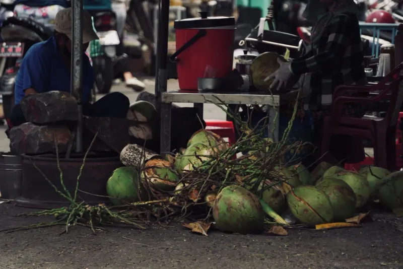 Street vendor splitting and preparing fresh coconuts by hand at an outdoor market stall in Thailand