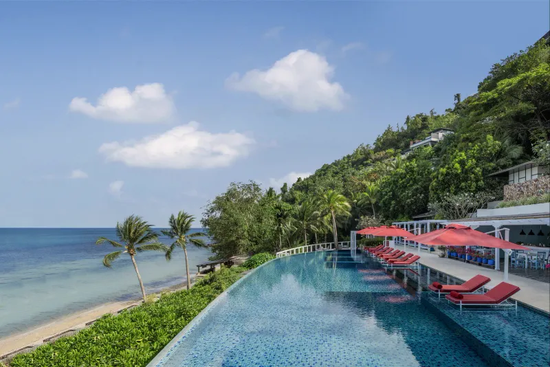Conrad Koh Samui main infinity pool with red loungers beside the bay and hillside villas