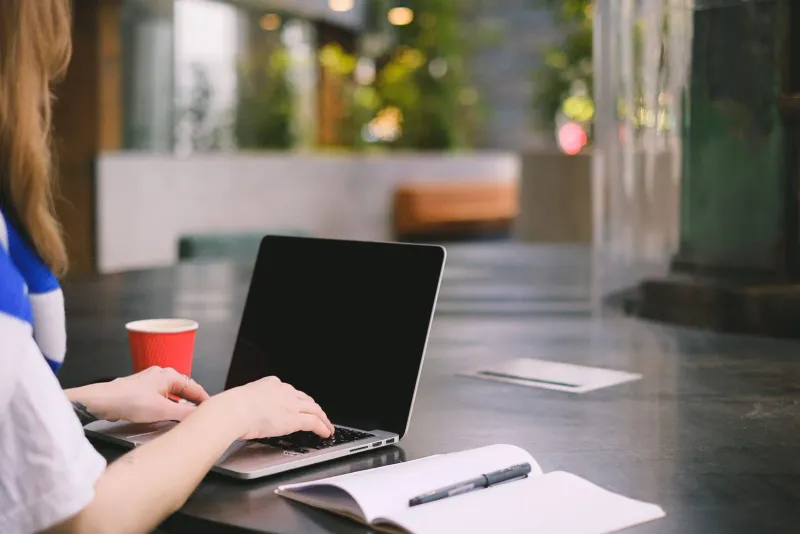 Person typing on a laptop with coffee and notebook, a common laptop-friendly cafe setup