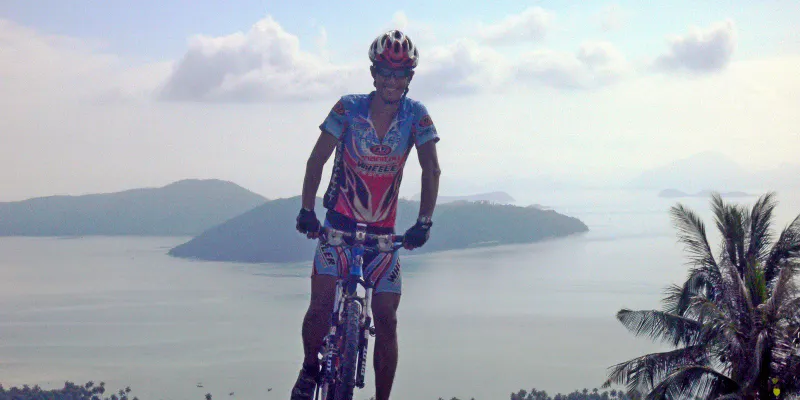 Cyclist in a red helmet stands on a hilltop with the sea and islands behind