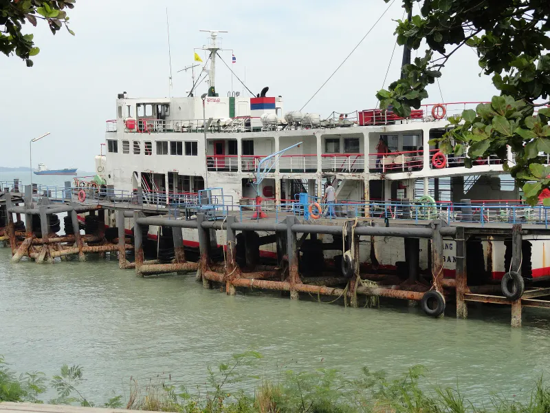 White car ferry moored at a rusty pier beside calm green water on the Gulf coast