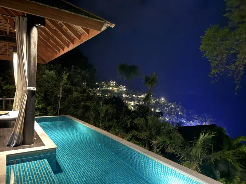 Villa plunge pool at dusk with terrace and distant lights of the coast below Four Seasons Resort Koh Samui