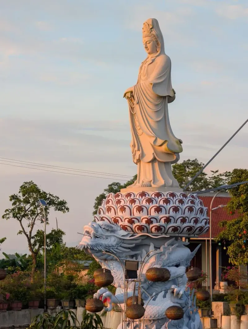 A stunning white statue of Guanyin gracefully stands atop a lotus at sunrise, exuding tranquility