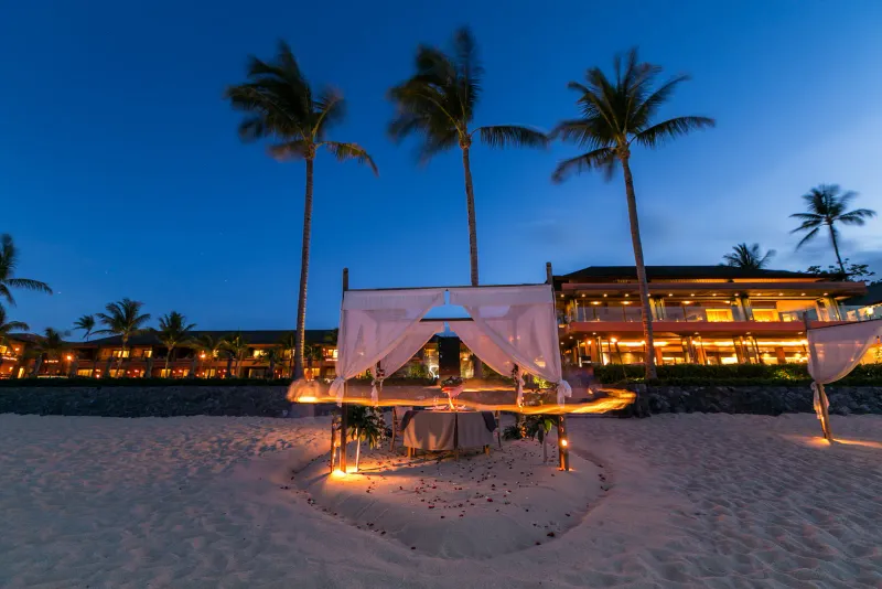 Candle-lit beach dinner setup with a canopy on the sand in front of the Hansar Samui restaurant at dusk