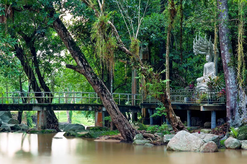 Buddha statue and footbridge over the river at Wat Namtok Hin Lat