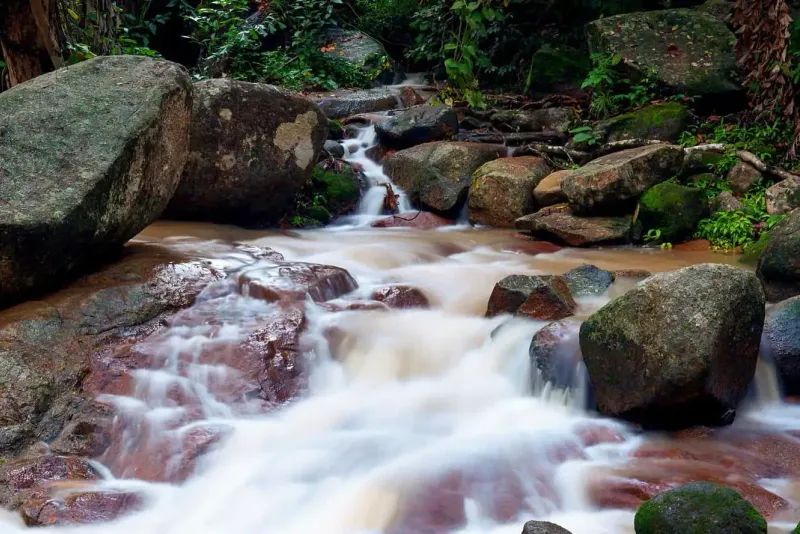 Muddy monsoon-season stream tumbling over granite boulders on the Hin Lad trail