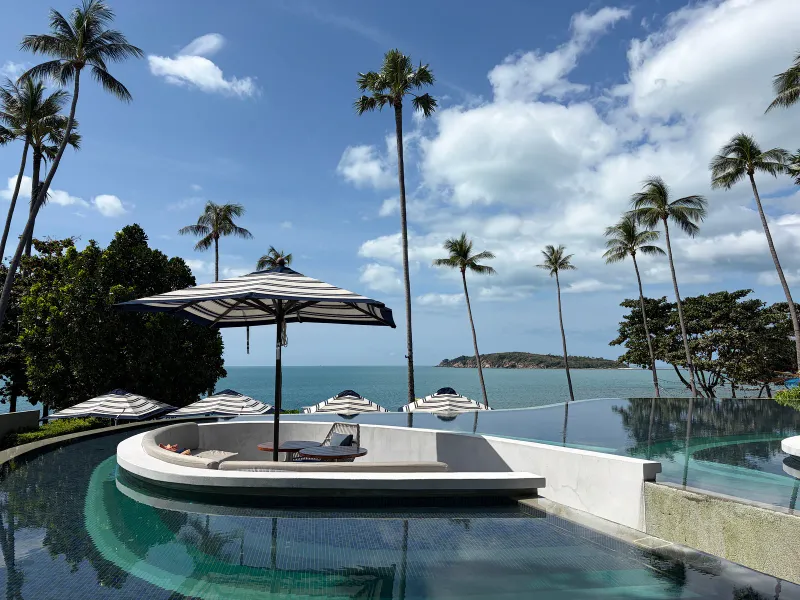 Sunken lounge seat with a striped umbrella inside an infinity pool at Hyatt Regency Koh Samui with palms and an island behind