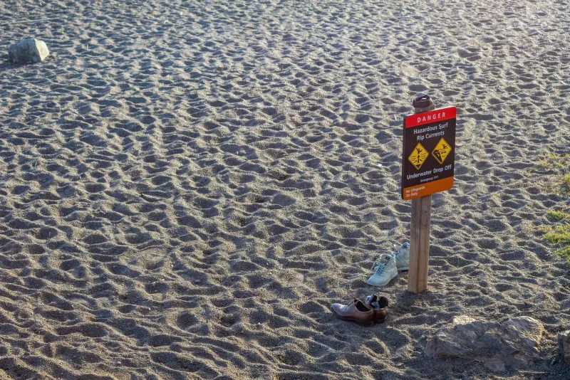 Beach warning sign with shoes left nearby on a sandy Thailand shoreline