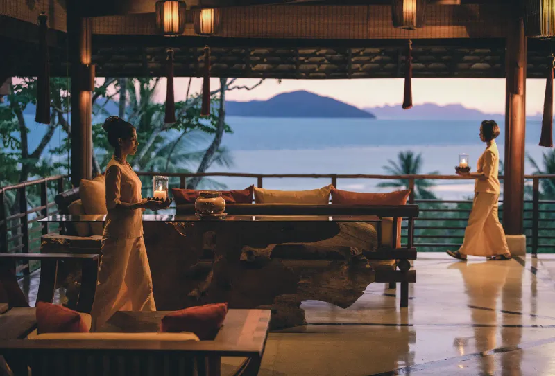 Staff carrying lanterns across the open-air dining terrace at Kamalaya Koh Samui at sunset
