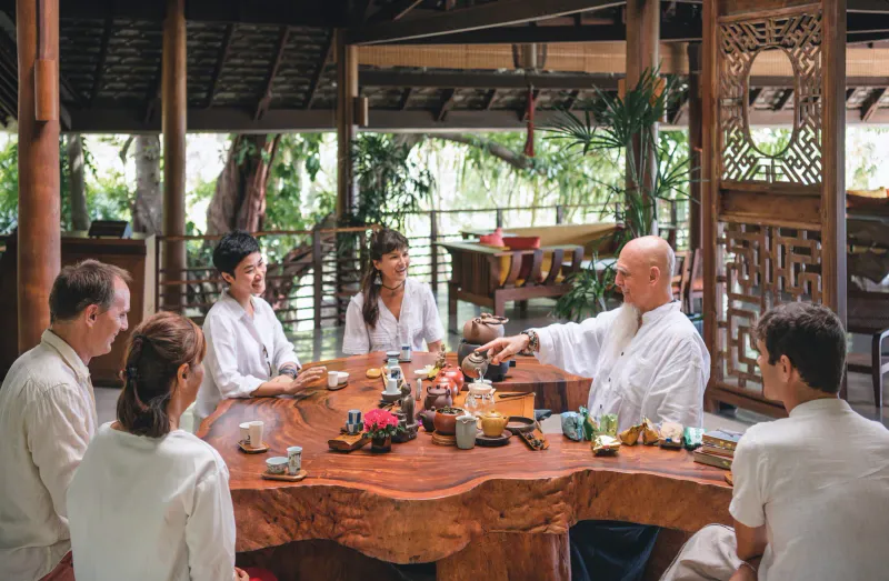 Guests and therapists sharing tea around a live-edge wooden table in an open Kamalaya Koh Samui pavilion