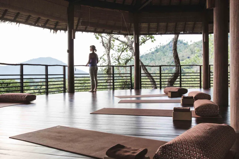 Open-sided yoga pavilion with mats and bolsters overlooking forested hills at Kamalaya Koh Samui