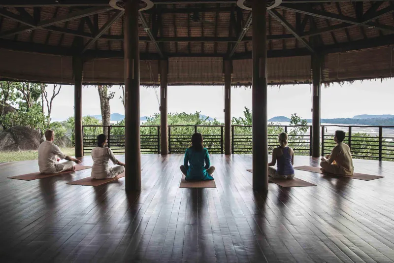 Guests seated on mats for a group meditation session in an open-air pavilion