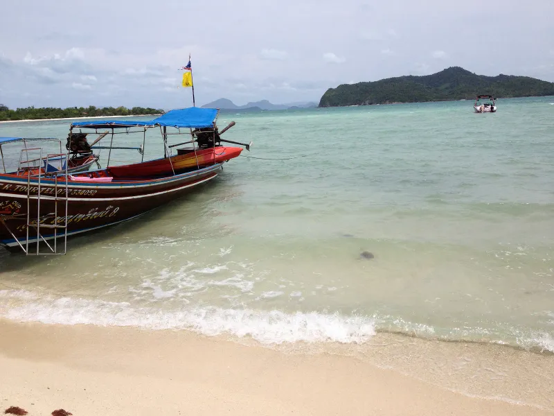 A longtail boat pulled up on the sand at Koh Madsum, shallow clear water around it