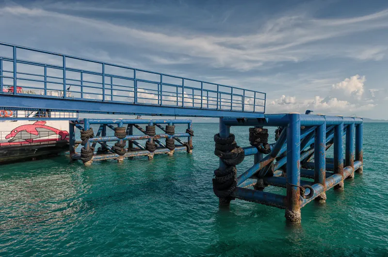 Blue steel ferry pier with tyre fenders over turquoise water and a ferry moored alongside