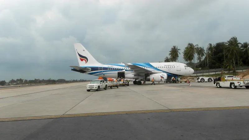 Bangkok Airways jet on the apron at Koh Samui Airport with palm trees behind