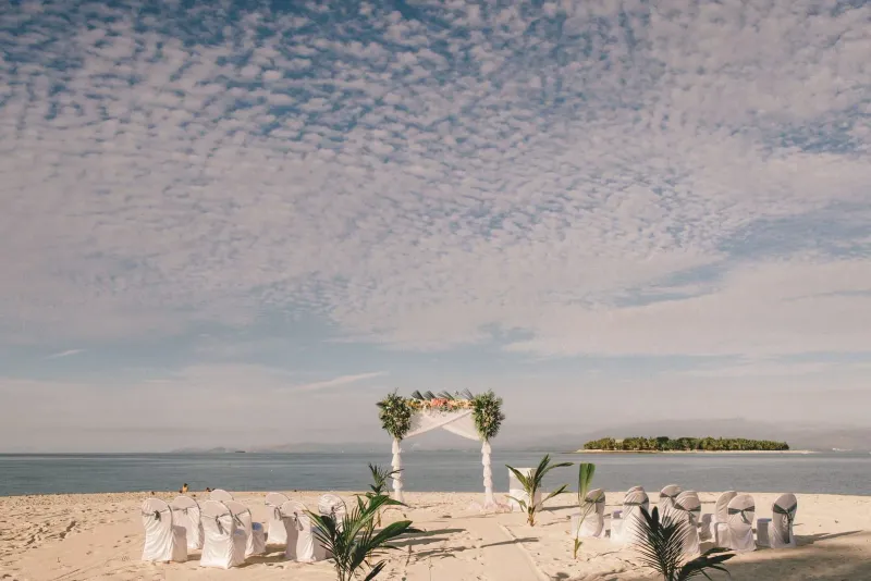 Tropical beach wedding ceremony arch decorated with white drapery and flowers facing the ocean
