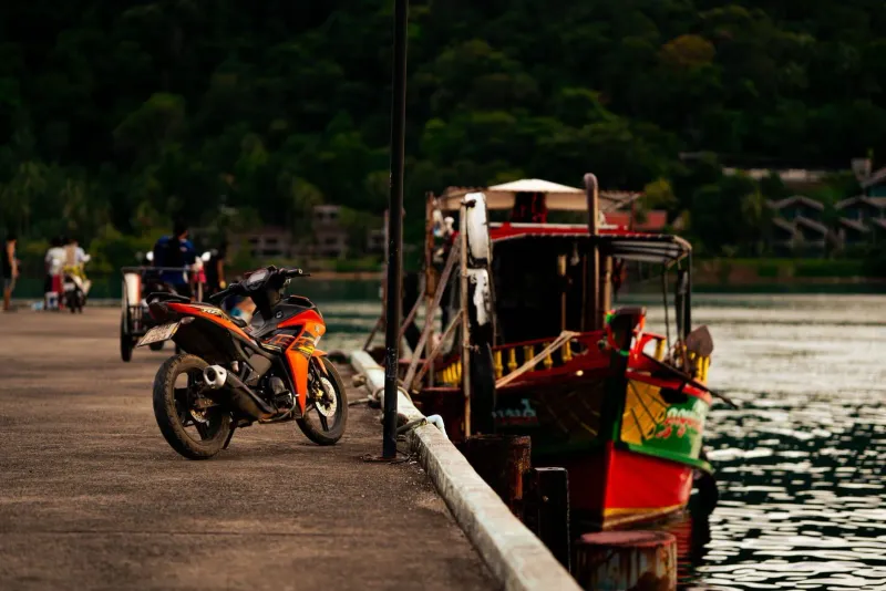 Motorcycle parked beside a colorful traditional boat at a pier near sunset on Koh Samui's south coast
