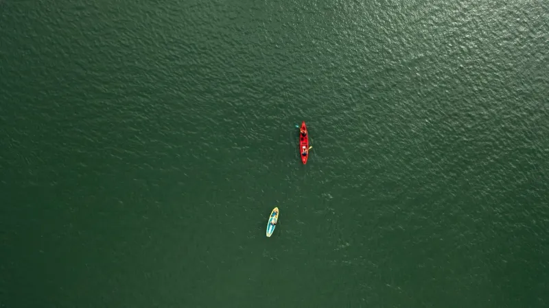 Aerial shot of a kayaker and a stand-up paddleboarder paddling side by side on calm open water