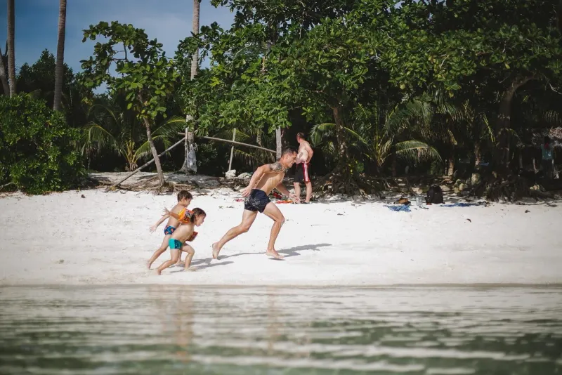 Father and two kids playing together on a calm Koh Samui beach in the afternoon sun