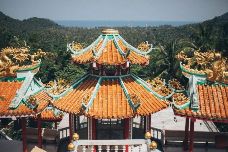 Ornate temple rooftops among lush greenery near a Koh Samui meditation retreat