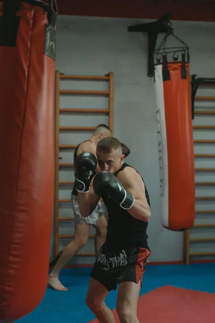 Two men practicing Muay Thai with punching bags in a gym, the drop-in class style at Jun Muay Thai Lamai