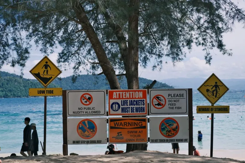 Multiple beach safety signs warning of marine hazards near the ocean shoreline