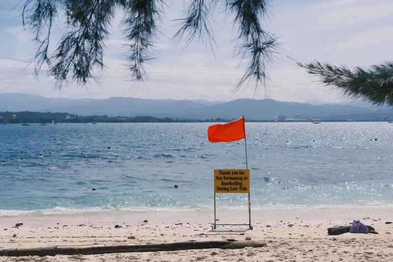 Red warning flag and low tide sign on a tranquil Koh Samui-style beach