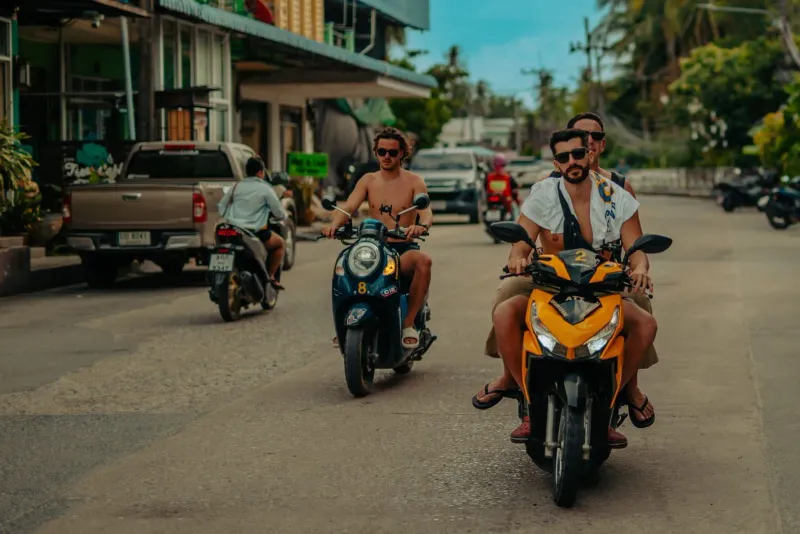 Group riding scooters along a tropical Koh Samui street on a backpacker day trip