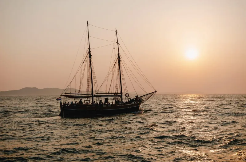 Traditional sailboat gliding across the ocean at sunset with mountains behind Koh Samui