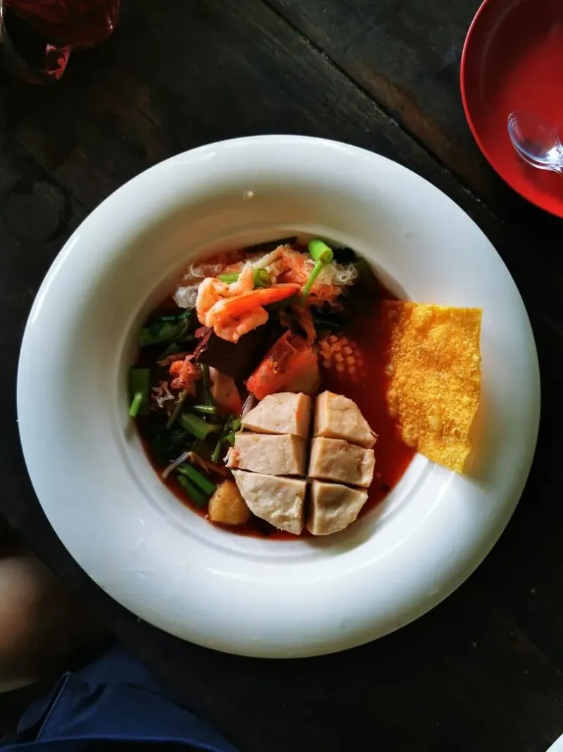 Thai tom yum soup garnished with fresh vegetables on a wooden table in Koh Samui