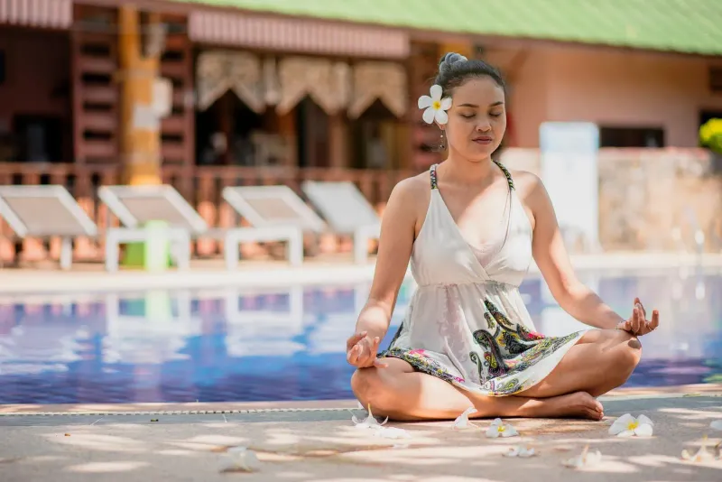Woman in white dress meditating beside a resort swimming pool on Koh Samui