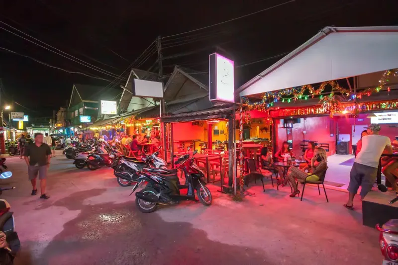 Bars and shops glowing along a night street on Koh Samui with parked scooters