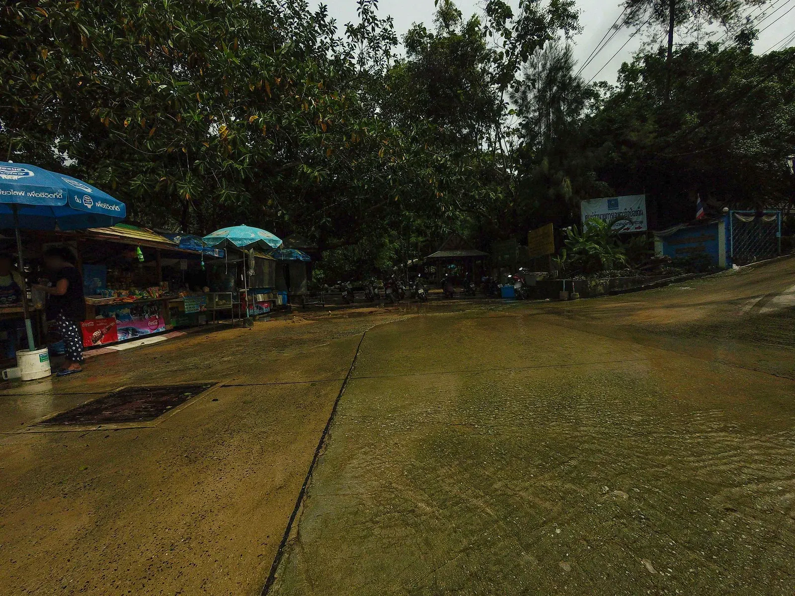 Motorbike parking area at the Hin Lad trailhead, shaded by tall trees