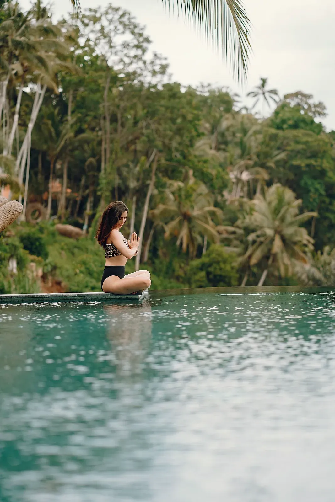 Woman meditating beside a pool in the jungle