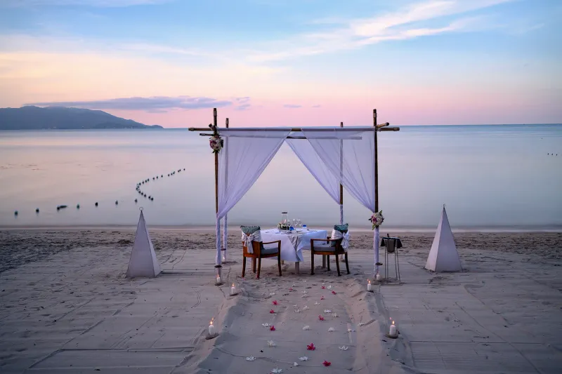 Private beach dinner set-up with a white canopy and lanterns at dusk at Melati Beach Resort