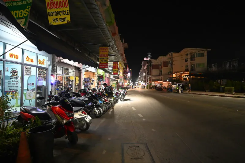 Row of scooters parked beside rental shops on a Thai street at night