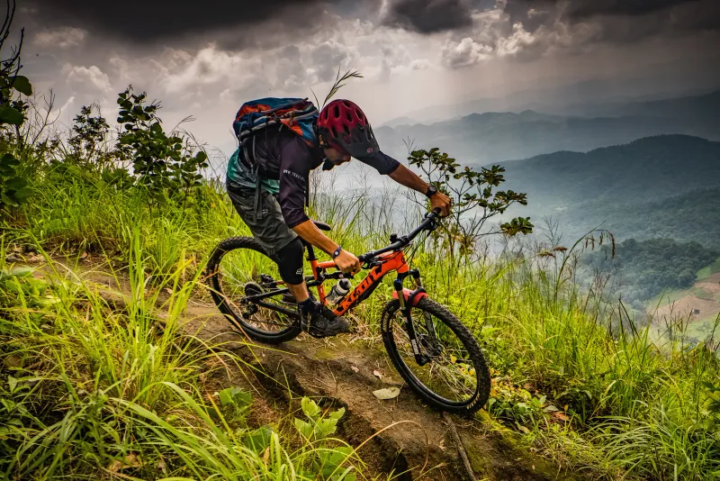 Mountain biker in a red helmet descending a grassy ridge trail above hazy hills